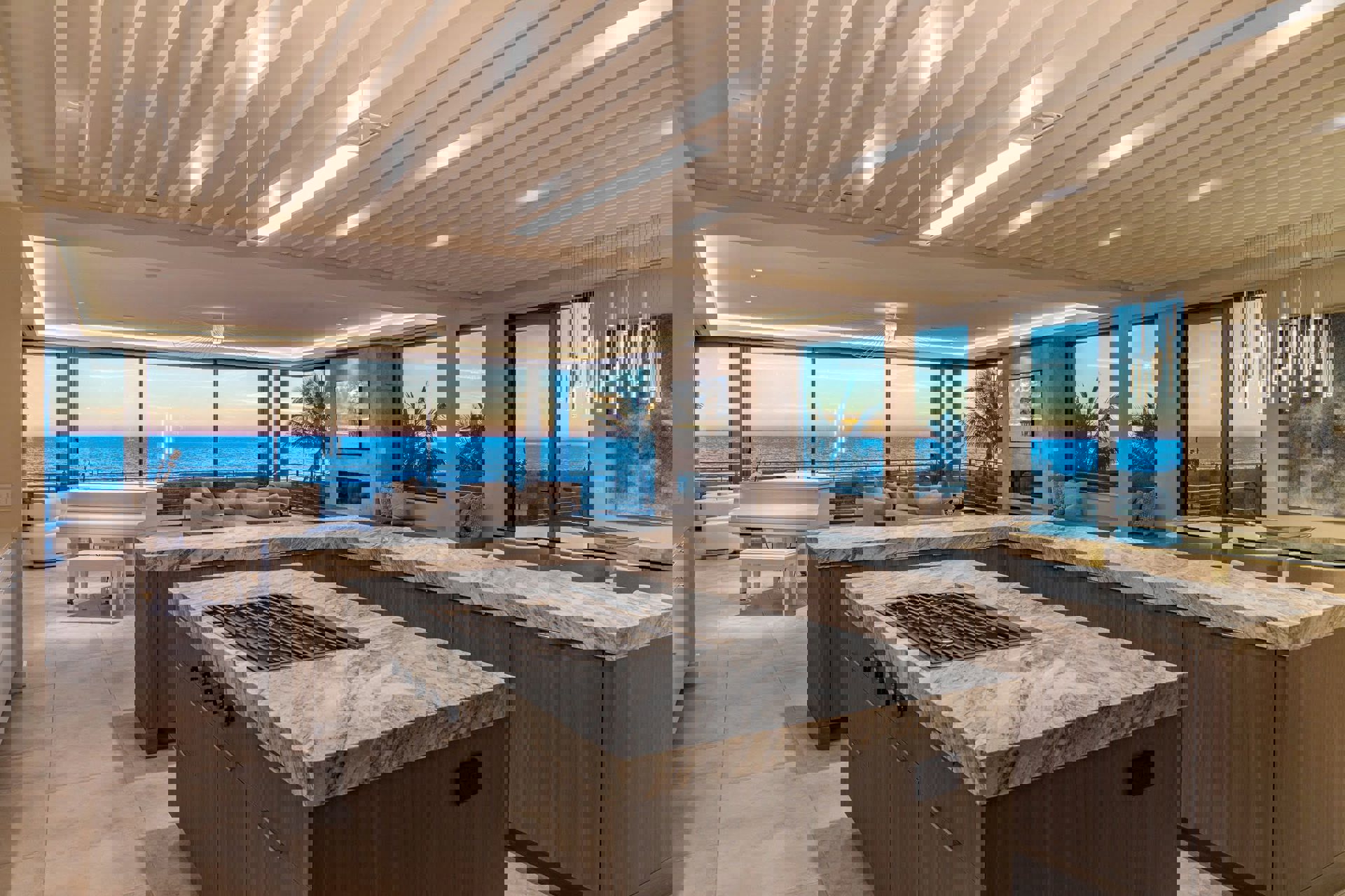 Luxury coastal home interior with large custom window systems and sliding glass walls framing an oceanfront sunset.