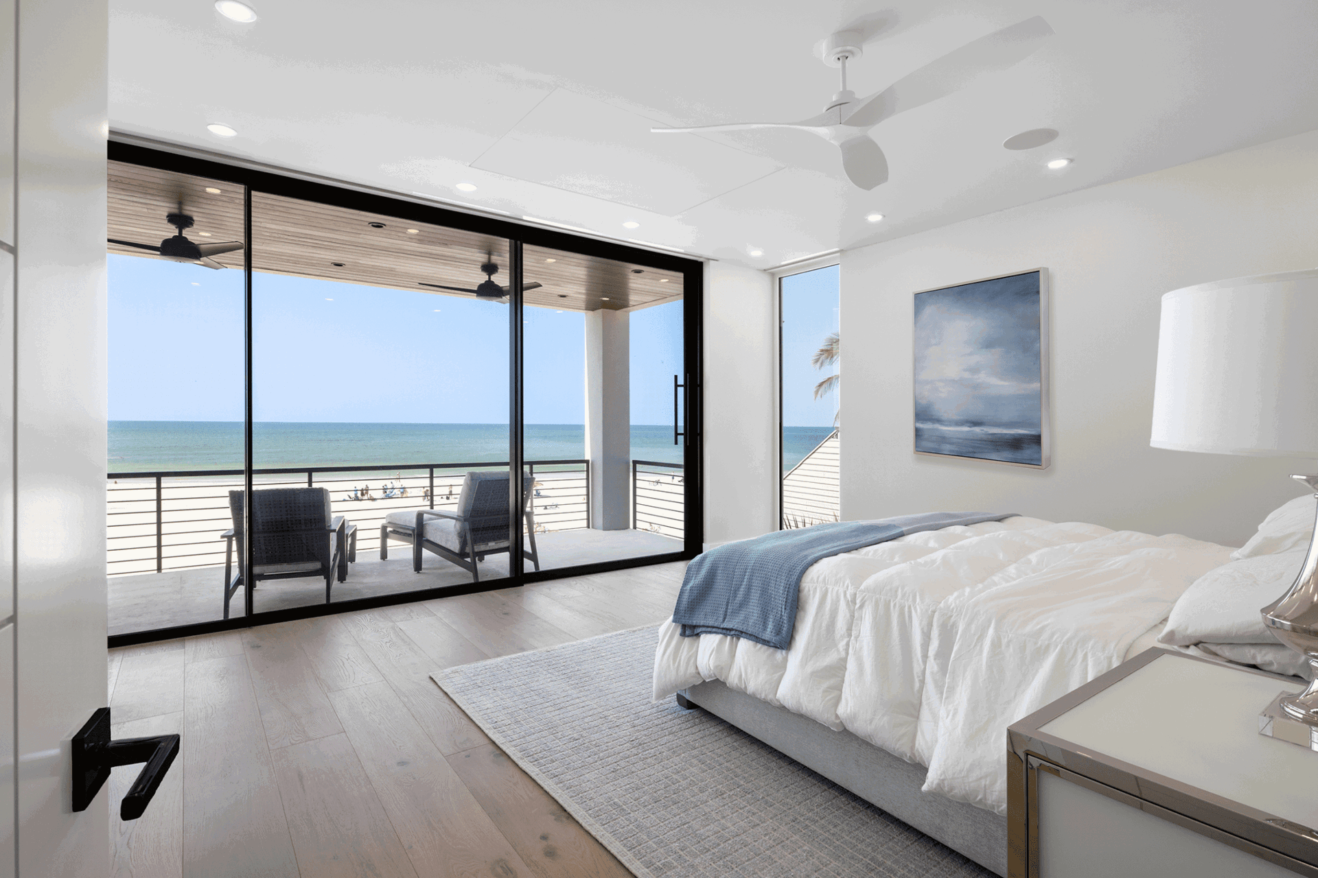 Modern bedroom with large sliding glass doors opening to an oceanfront balcony and panoramic beach views.