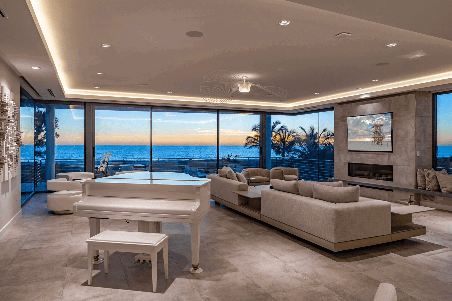 Contemporary living room featuring floor-to-ceiling sliding glass doors framing a panoramic ocean sunset.